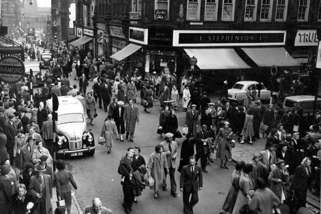 Looking south east along Kirkgate from Central Road in July 1956. The Central Buildings created by architect Thomas W Cutler in 1901. The shops and offices are a Bold Q Anne revival in brick with brown faience giant rusticated pilasters between the shopfronts surmounted by brackets with obelisk finials. Fine wrought iron gates to the inner yard. I. Stephenson Ltd. butchers, J. Sears and Co. (True Form Boot Co.) Ltd. boot and shoe dealers, Chic Modes Ltd. ladies outfitters, Farm Stores Ltd. pork butchers and the Yorkshire Penny Bank shown.