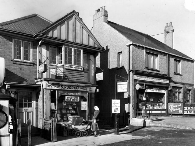 Shops on Harrogate Road in February 1952. Number 403 is R.S. Rudd, Newsagents and Postoffice. Number 405 is J. Eamonson, Household Stores. A woman with a child and pram stands outside. Advertisements on the shops are for Capstan tobacco, Lyons ice cream, Wills cigarettes, Players cigarettes and Cadbury's. A petrol pump is partly visible on the left.