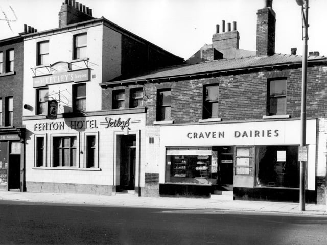 Woodhouse Lane in March 1966. On the left edge of this view, part of the premises of Walter Thomas Castelow's pharmacy at number 159 can be seen. This is now a bar called Strawberry Fields. Moving right, number 161 is a Tetley's Public House, the Fenton Hotel with Herbert H Baxter as the landlord. It was built in 1853 and is still open today. Number 163 is a bakery and coffee bar owned by Craven Dairies.