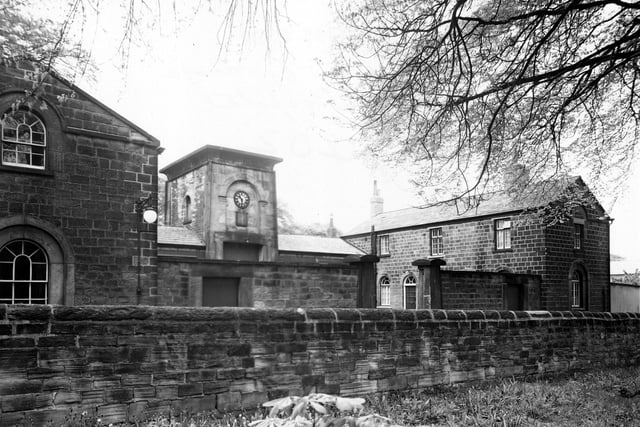 The stables on Gledhow Park Drive. The centre building has a clock on the front. A stone wall and field are in the foreground. A lamp is on the side of a building and large stone gateposts are visible. It was in the grounds of the former Chapel Allerton Hospital. Pictured in May 1950.