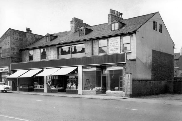 Shops on Dewsbury Road including a modern mens outfitters on the right at number 192. Ladders inside the shop suggest a refit in process however the sign above the shop still promotes 'Honest and friendly service' with 'All goods priced in plain figures'. On the left at number 194 is a grocers with a ginnel on the left giving access to the rear of the shops. On the far left an advertisement is painted on the rear wall of a building promoting A. Wrights garage. Pictured in August 1964.