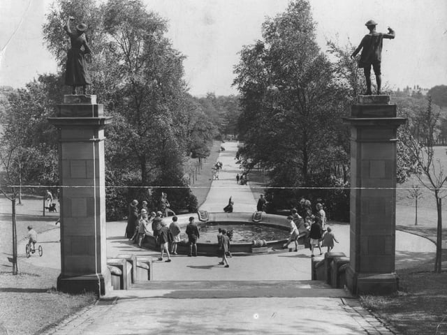 Roundhay Park looking down along Centre Walk, also known as Middle Walk, from the path leading up to the Mansion in May 1934. Statues of a woman and a man stand on top of posts at either side of a flight of steps leading down to the circular fountain. The tree-lined Centre Walk continues beyond this into the distance where it leads to Waterloo Lake.