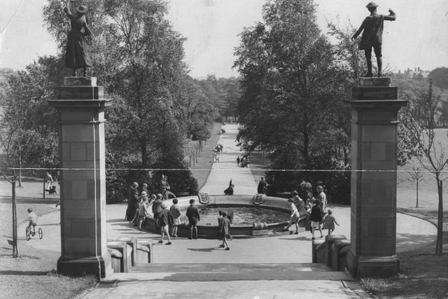 Roundhay Park looking down along Centre Walk, also known as Middle Walk, from the path leading up to the Mansion in  May 1934. Statues of a woman and a man stand on top of posts at either side of a flight of steps leading down to the circular fountain. The tree-lined Centre Walk continues beyond this into the distance where it leads to Waterloo Lake.