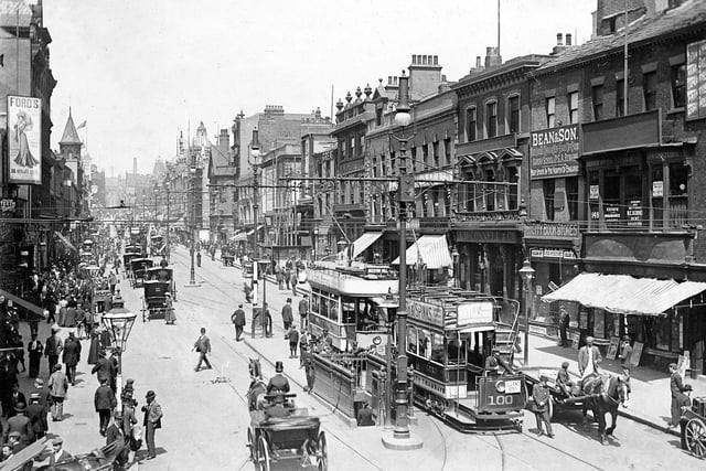 Briggate with trams and a variety of horse drawn vehicles. Just out of view to the right is the junction with Duncan Street. The shops in view include J.W.Bean and Son, bookseller at number 149, with signs in the window stating 'selling off' and 'under notice to quit'. Moving along Briggate, A. McConnell, wine and spirit merchants, are next to Beans, then Maypole Dairy Co. and Lockhart's tea rooms beyond that.
