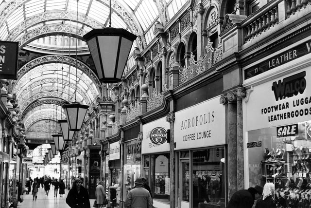 The County Arcade looking in the direction of Vicar Lane in July 1982. The arcade was designed by renowned Theatre and Music Hall architect, Frank Matcham, and built between 1898 and 1903. The arcade was built on the former site of Cheapside and the Shambles including Queen Victoria and King Edward Streets. In this 1980s image it is possible to see many fine details such as the ornate cast iron first floor balconies and the columns and pilasters of Sienna marble. Some of the shops & businesses seen include Saltaire Galleries, Waynes shoe shop, Acropolis Coffee Lounge and, at the right edge, Walco Footwear, Luggage and Leathergoods. The entrance to Queen Victoria Street is behind the women looking in the window of Saltaire Galleries, left of centre.