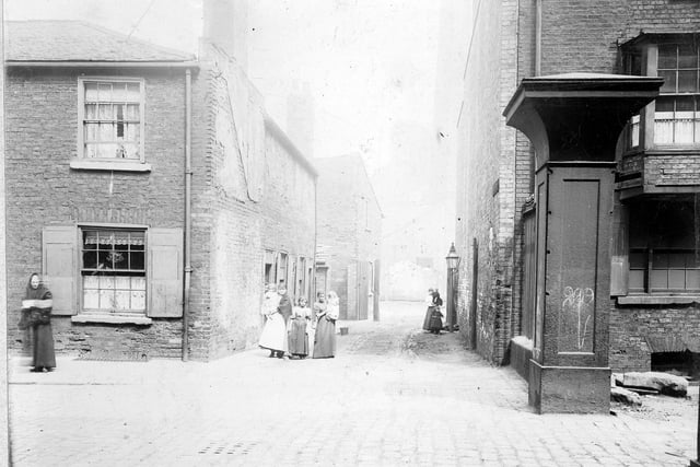 The entrance to Bow Court prior to the Swinegate/ Sovereign Street improvements. Premises shown are residential with sash windows and wooden shutters. On the right a steel gateway, the entrance to to Albion Works. Several women and children are standing in the foreground. Pictured in July 1902.