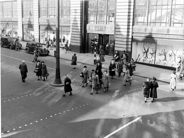 Pedestrians cross the road outside Lewis's (Leeds) Ltd. department store in March 1949. A ladder is leant against the store and cars are parked outside.