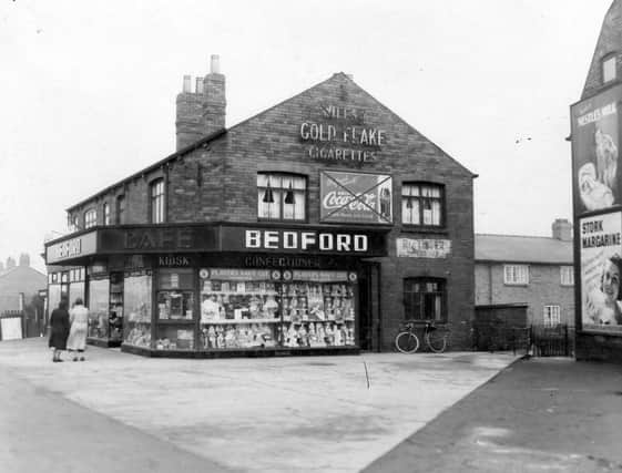 Bedford's confectioner's shop taken from Middleton Park Circus in February 1939. The substantial shop which was situated on the corner of Middleton Park Road and Circus has windows filled with confectionery. There is a neon advertisement for "Gold Flake" and a hoarding for "Coca Cola" on the side of the building, though these have been crossed through by the City Engineers. Other advertising hoardings are for "Nestle's Milk" and "Stork Margarine". Women are chatting in front of the shop and there is a bicycle leaning outside.