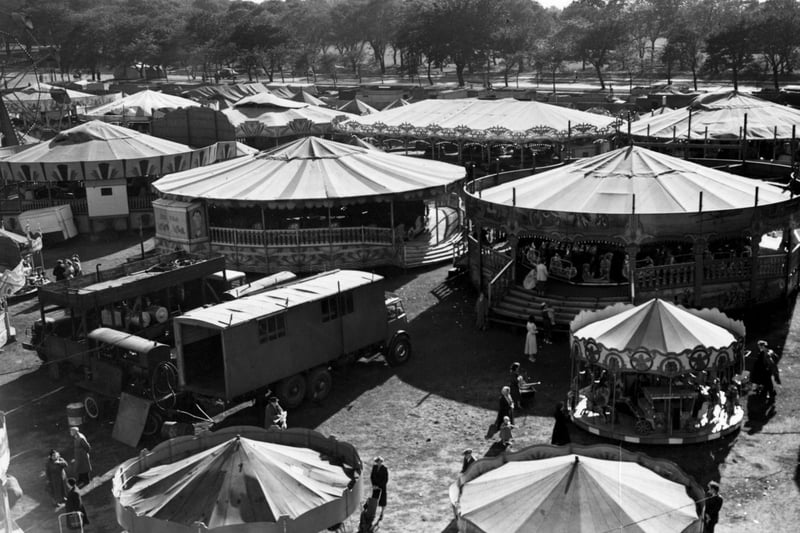 Woodhouse Feast on Woodhouse Moor in September 1955. People can be seen on or near various rides and stalls. Woodhouse Lane is visible in the background.
