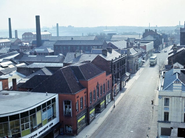 A view looking southwards along Queen Street, Morley, from the bell balcony of Morley Town Hall. The rooftops of buildings in the area around Peel Street and Hope Street are shown, plus the fronts of shops on Queen Street from the Co-op Emporium to the new Post Office. The tall chimneys on the left belong to Peel Street Mills (nearest), Peel Mills (next), then Melbourne Mills and Melbourne Street brickworks. Pictured in April 1965.