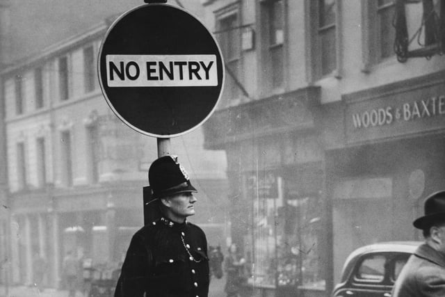 A policeman stands under no entry sign on Commercial Street. The Woods & Baxter shop is in the background.