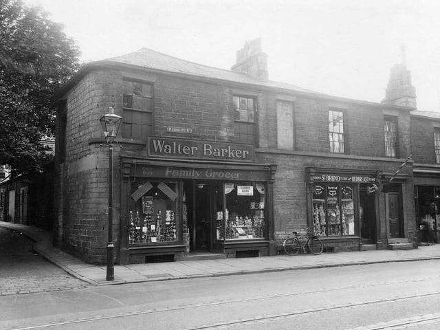Harrogate Road at the junction with Short Lane in August 1935. Here is a row of stone built shops with slate roofs. On the corner is W.Barker, Family grocers, Est 1844. Next is J.E.Bolton, Hairdresser. In the window of this shop there are advertisments for St.Bruno and Redbreast Flake, pipe tobaccos. A gas streetlamp stands on the pavement and a trademans bike leans against the wall.