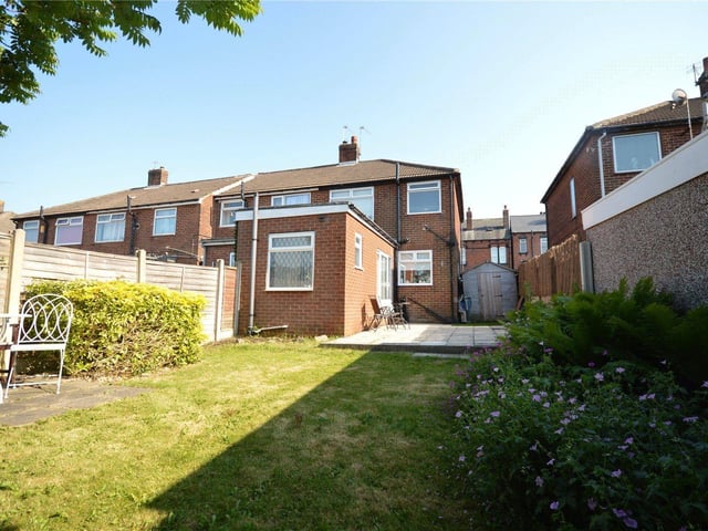 A landscaped rear garden features a patio and a lawn, with an array of mature plants and shrubs surrounding the border.