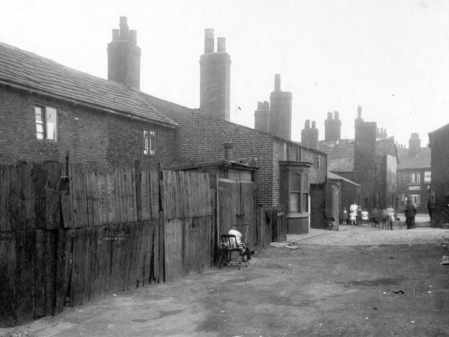 Finny Yard was a conglomeration of properties. To the left, fencing and shed, child in push chair. A group of children stand near the yard entrance.