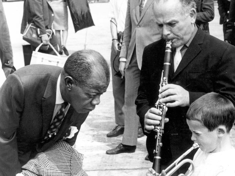 Jazz trumpeter Louis Armstrong is seen arriving at Leeds and Bradford Airport. He was met by seven-year-old Enrico Tomasso from York Road, playing 'Basin Street Blues' with his father Ernie. Louis was due to appear at Batley Variety Club