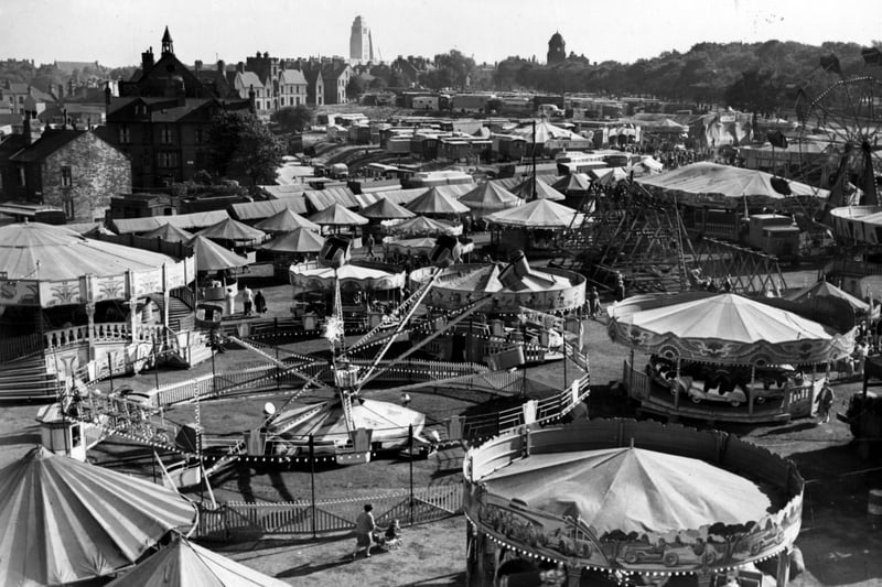 Woodhouse Feast fair on Woodhouse Moor. People can be seen on or near various rides and stalls. Crossfield Street, Raglan Road and Leeds University can be seen in the background. Pictured in September 1955.