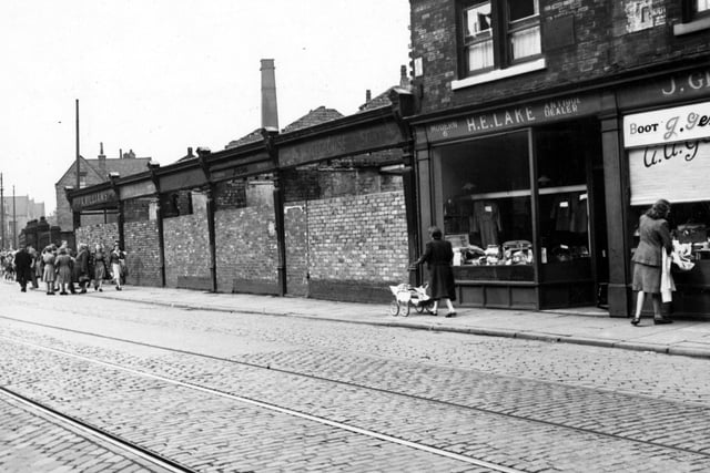 The north side of Meanwood Road pictured in June 1948 showing ruins and H.E. Lake, antique dealer. There are several pedestrians on the street, which has tram lines.