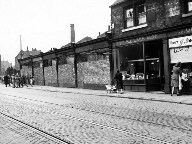 The north side of Meanwood Road pictured in June 1948 showing ruins and H.E. Lake, antique dealer. There are several pedestrians on the street, which has tram lines.