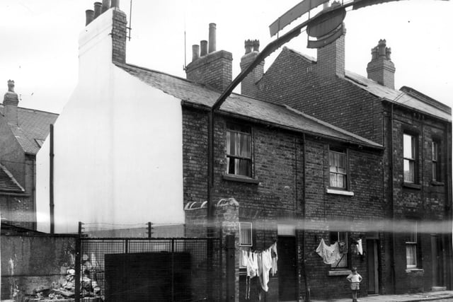 On the left is part of the yard belonging to the premises of the Leeds Paint Manufacturing Company Ltd, Gem Works. There is a large arched sign over the road with the name of the company. The houses seen are back to back brick terraces and they number from the left 8, 6 & 4 Marquis Street. A small boy poses for the camera outside the window of number 6.