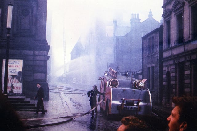 A fire engine and crew at work to extinguish the fire which spread through Morley Town Hall in August 1961 after starting in Albert Mills behind. The fire engine is parked in Wellington Street at the side of the Town hall, with Lloyd's Bank seen on the right. Despite the efforts of the fire crew the dome of the Town Hall suffered severe damage and had to be replaced.