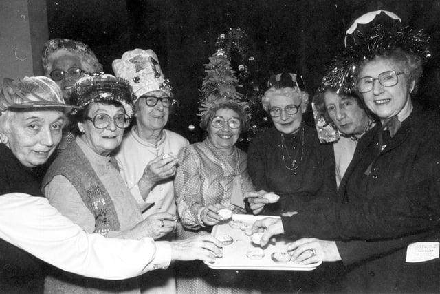 A group of ladies in party hats enjoying mince pies at the Epiphany Lunch Club Christmas Dinner held in the Epiphany Hall of the Church of the Epiphany on Beech Lane in December  1984. The dinner was followed by a Christmas show including a Victorian drawing room party with traditonal Christmas songs. It was an opportunity for representatives of the Anglican, Methodist and Catholic churches to get together. The Epiphany Lunch Club was a weekly event, held each Friday. It provided a two-course meal, followed by tea and biscuits, for pensioners at a cost of 65p.