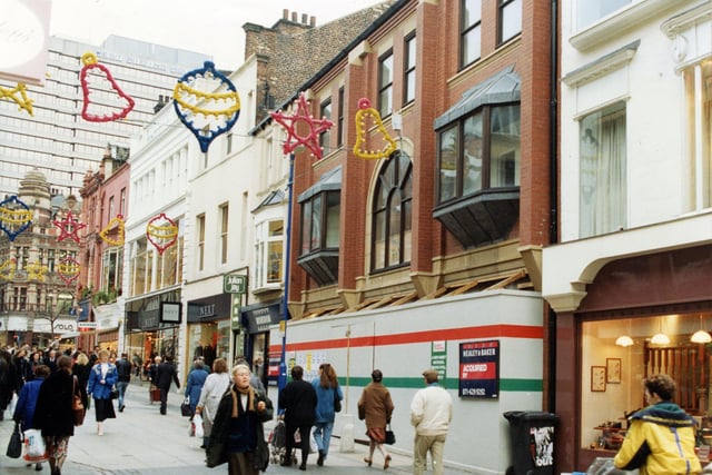 Commerical Street in November 1990. Shops in focus include Cable & Co. menswear, Monsoon ladieswear, with Julian Jay hair above, Next ladies and menswear and Ratners jewellers. Solo ladieswear can be seen beyond the junction with Lands Lane. West Riding House can be seen in the background.