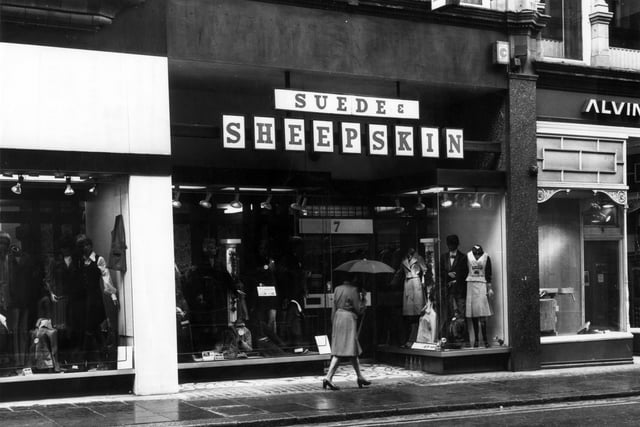 A woman with an umbrella is walks past the Suede and Sheepskin shop on King Edward Street in May 1976. The shop was here from circa 1963 to 1983. To the right is Alvin Morris Ltd., decorators' supplies showroom, which was here from 1971 to circa 1976. They also had works premises in Hunslet.