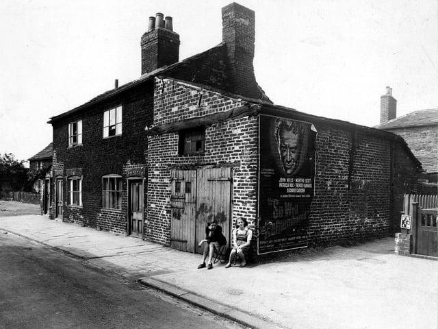 Two young girls are sat in front of a garage on Town Street looking at the camera. Pictured in July 1947.