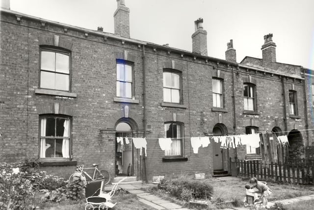 Three back-to-back properties on Parsonage View. A bicycle and a pushchair can be seen outside number 19 while a girl plays with her own pushchair further along the path. These gardens backed onto allotments with passageways such as the one on the right edge giving access to Main Street. Pictured in August 1966.