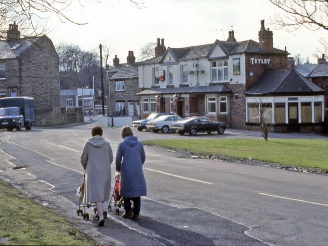 Finkle Lane from Gildersome Green, showing The Junction pub on the right in March 1984. Two women are pushing children in pushchairs in the foreground. The gable end of a terrace of houses on The Nooks is seen on the left.