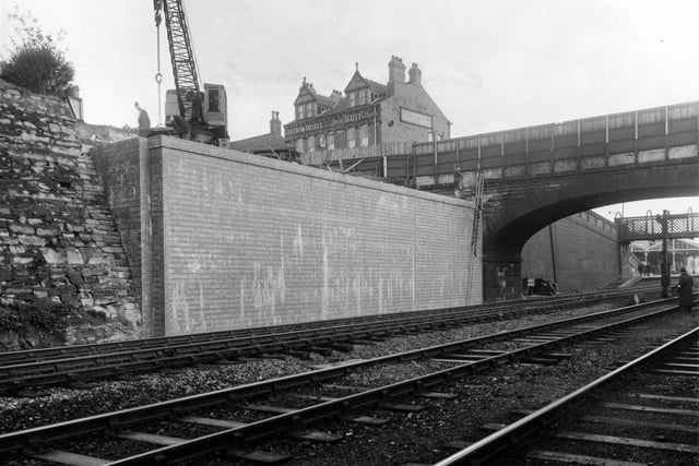 A view looking north along the railway and under the bridge at the west end of Cross Gates Station. A small crane can be seen on the left side of the bridge. In the background one can see the Station Hotel on Station Road. A long ladder is leant against the bridge and a man looks to be carrying out survey work on the bridge.