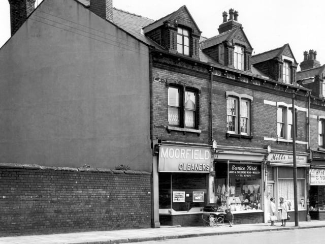 Pictured in June 1965, from left, is Moorfield Cleaners with a sign in the window which states 'Ladies Bargains this week! Costumes and Jumper Suits only 4/11d' (just under 25p). Costumes refer to a ladies skirt and jacketed suit, while a jumper suit was a knitted top and skirt. Moving right, a child holds onto a pram outside the entrance to Eunice Hirst's Ladies and Childrenswear. The window is crammed with women's tops and jumpers and girl's dresses. Two women chat outside Mills Hair Fashions and on the right is Simpkin and Young, radio and television engineers.