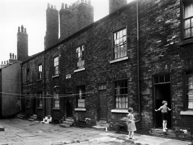 A view of Providence Court, on the left the gable end of number 7 Queen Court can be seen, then 7 Providence Court. Moving right numbers follow in ascending order to 12, where a boy is in the doorway. A girl waiting for him. At the back of numbers 7 to 10 was the side of 6 Queen Square. These were small cottages usually called one up, one down, referring to one room on the two levels. Pictured in August 1959.