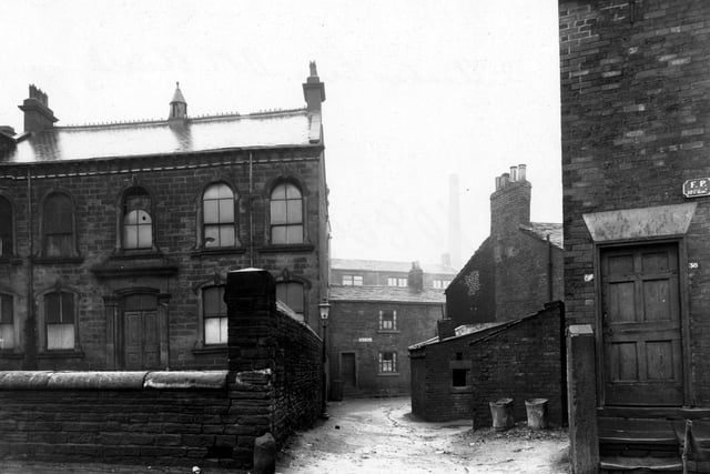 Looking north at the entrance to Back Fold from Theaker Lane in January 1948. On the right is number 38 Theaker Lane, with the Methodist Chapel enclosed within a stone wall on the left. Back Fold is central, (an unmade road with a gas streetlamp and two metal dustbins in it).