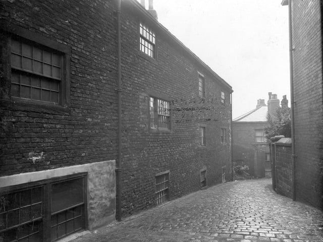 The rear of housing known as Wasp's Nest in July 1936. A street paved with stone sets leads down backs of houses, towards another unidentified street.