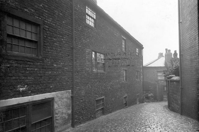 The rear of housing known as Wasp's Nest in July 1936. A street paved with stone sets leads down backs of houses, towards another unidentified street.