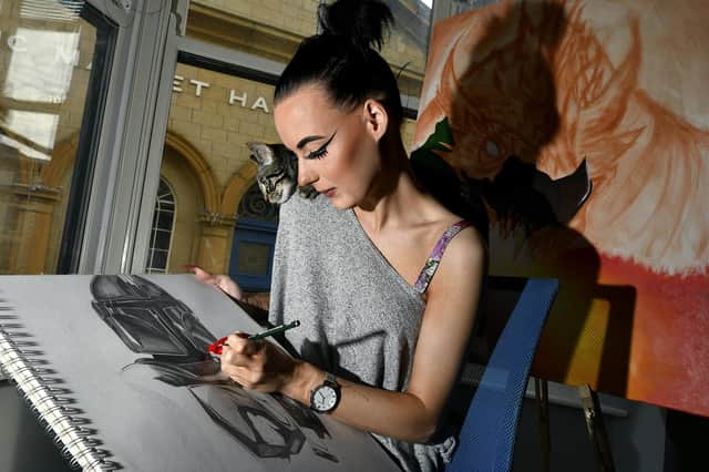 Artist Chloe Alexia works on her Mandalorian drawing as Morpheus the kitten looks on