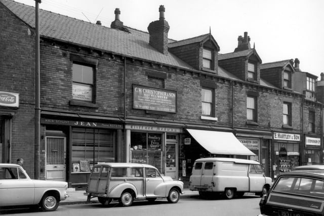 From left is Jean, hairstylist pictured in June 1965. Clifford Medway is at number 156 for watch repairs and jewellery. Above this is an advert for C.W. Christopher & Son, plumbers, based at number 138 Tong Road. Continuing right, the shop with the awning is Dobson's grocers at number 154, with Ackroyd & Son, electricians, at number 152. On the right are E. Hartley & Son, grocers (150), then I. Stephenson Ltd, butchers (148) which was one of several branches across the city.