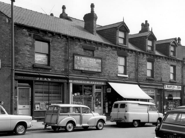 From left is Jean, hairstylist pictured in June 1965. Clifford Medway is at number 156 for watch repairs and jewellery. Above this is an advert for C.W. Christopher & Son, plumbers, based at number 138 Tong Road. Continuing right, the shop with the awning is Dobson's grocers at number 154, with Ackroyd & Son, electricians, at number 152. On the right are E. Hartley & Son, grocers (150), then I. Stephenson Ltd, butchers (148) which was one of several branches across the city.