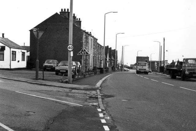 Bradford Road in East Ardsley, from the junction with Chapel Street, seen on the left, and looking south-east. On the left can be seen a small white building, in use as a cafe, and now a Chinese take-away restaurant. Beyond the parked cars are numbers 58 to 48 Bradford Road, and beyond them, the building of the former East Ardsley Boy's School, in use as a youth club from around the late 1960s, and demolished in the early 1990s. To the right can be seen trucks passing a builder's yard, and in the distance is a Texaco filling station, now a BP garage.
