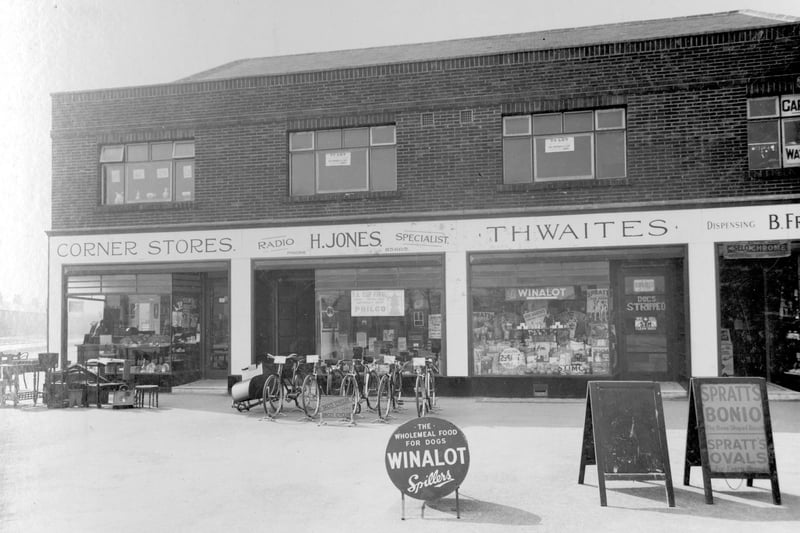 Terminus Parade, a rwo of four shops, on Station Road pictured in April 1936. The left corner stores is the business of Ivy Hodgson, items of furniture are outside the shop. Next right H.Jones selling radios and bicycles, a number of bicycles are on display. Thwaites pet supply store has advertising boards for products Winalot and Spratts. Extreme left is Bernard Freeman chemist