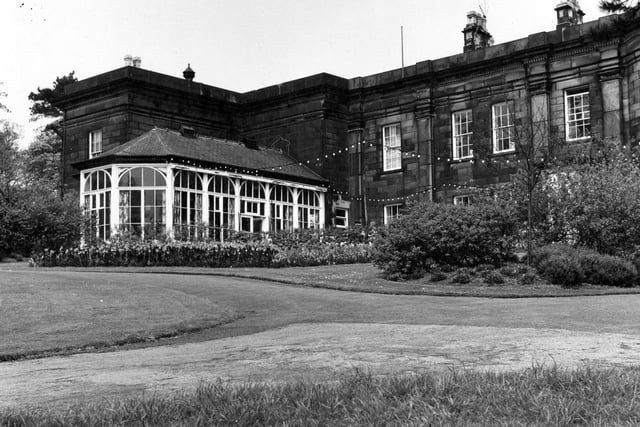A side view of The Mansion showing conservatory pictured in June 1967. The lawns and gardens in the forground of the image have fairy lights strung across them.