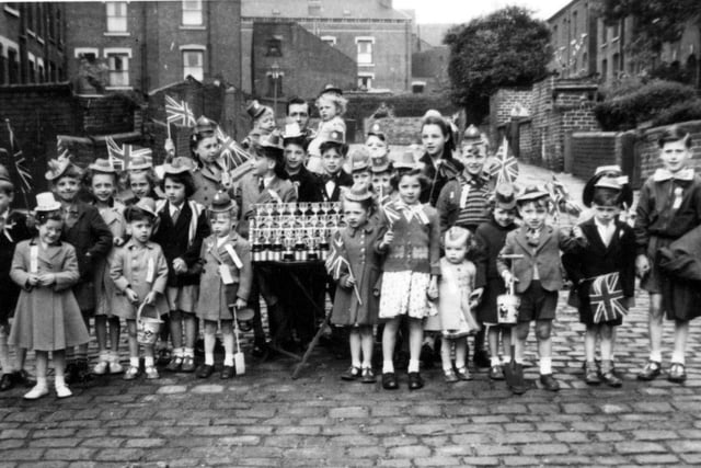 A group photograph showing the children of Greenmount Place and Greenmount Street in Beeston with Coronation silver cups, before they set off on an outing to Redcar in celebration of Coronation day.