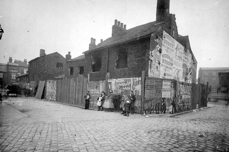 The demolition of property for improvements to Park Lane in June 1897. The site is fenced off and a group of children posing for camera. One of the posters is advertising Whitbreads Stout 2 1/2d (approx 1p).