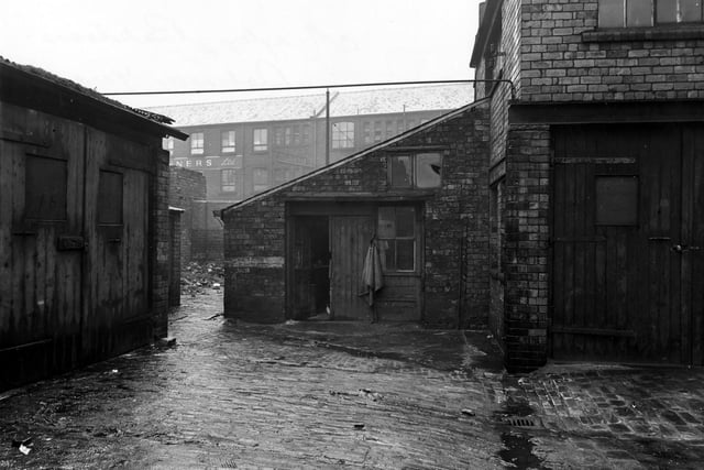 Midgley's bakers, Balm Road in Febraury 1951. Padlocked wooden garage doors are on the left and right. The wooden back door to Midgley's is open and a drain grate is visible on the cobbled yard.