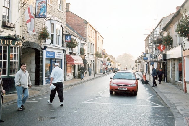 High Street in 2003. The Angel Inn is on the left. This is one of the oldest coaching inns in Wetherby it was established before 1700. It was one of the two posting inns, where the mail coaches would stop. The entrance to the yard where horses would be stabled is to the right of the pub window, under the sign.