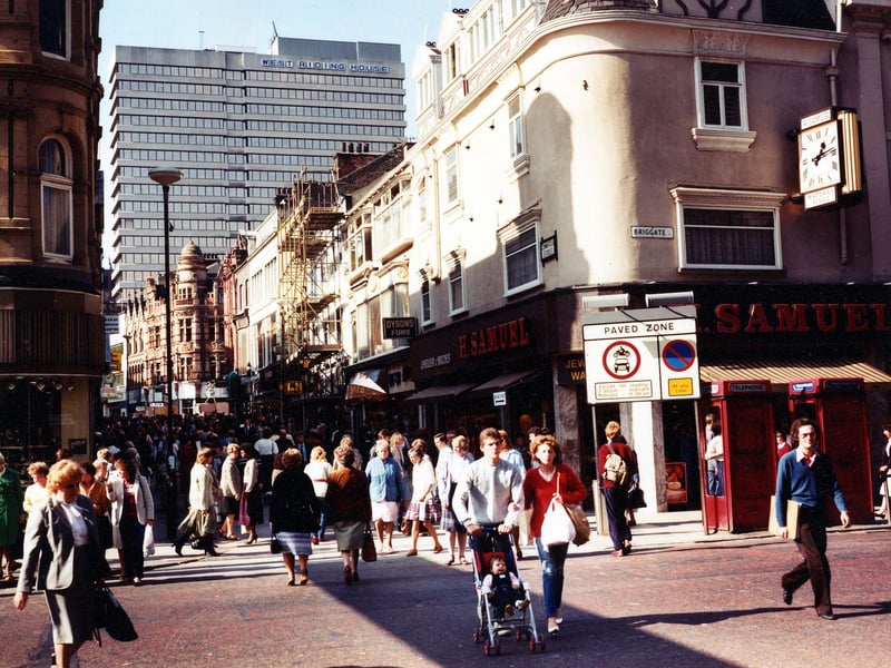 A crowded Commercial Street from Briggate. On the right, two red telephone boxes can be seen in front of H.Samuel, jeweller, which has a large clock on the wall outside. The shop just visible is Manfield footwear.