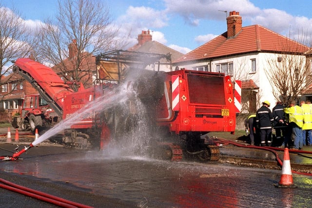 A road planer hit a gas main on Park Road in Glasshoughton and set on fire in March 1996. Water monitors cool the machine as flames lick the underside. Workmen dig for the main to relieve pressure.