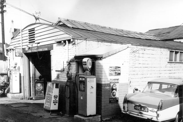 A car garage on Green Lane with Fina Super petrol pumps outside with petrol is 4'10 a gallon. A sign above the door reads J.R. Shute licensed petroleum spirit store. Signs on the side of the garage promote Chapion dependable spark plug service and Ferodo brake testing service.
