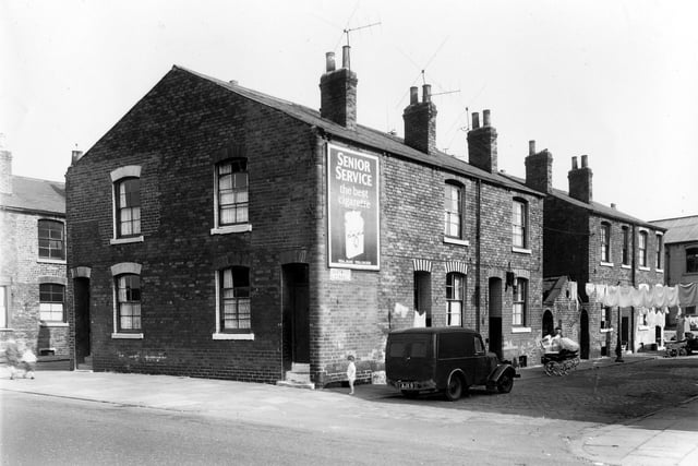 Clothes are visible hung on lines stretched across the street while prams stand facing house entrances on Eastwood Street in September 1959. On the left of the image are two houses located in the gable end of the terrace, numbers 44 and 46 Cross Stamford Street.